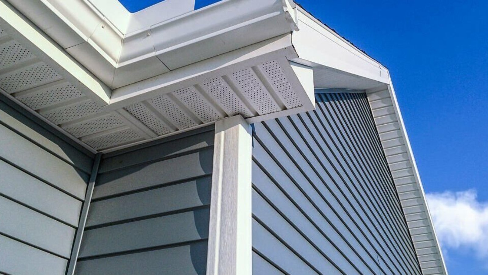 A low angle view of soffit, gutters, downspout and vinyl siding on a new home. Blue sky is in the background.