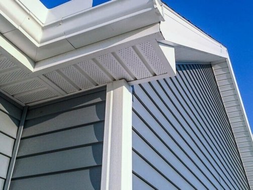 A low angle view of soffit, gutters, downspout and vinyl siding on a new home. Blue sky is in the background.