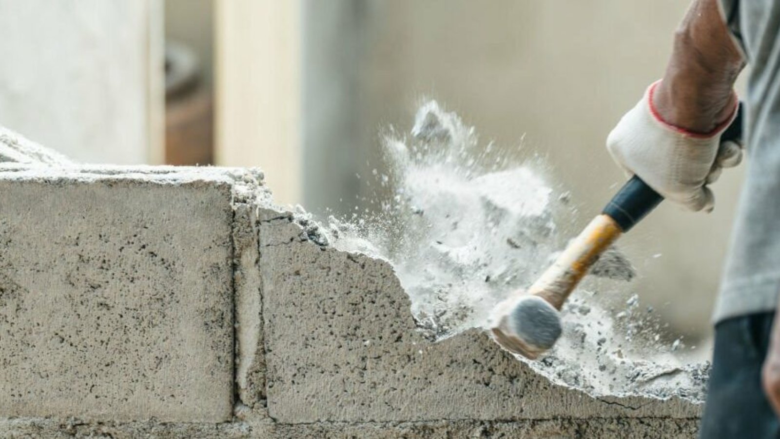 Hand of worker using hammer smashing and demolish on brick block wall at construction site