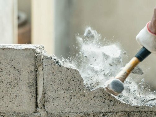 Hand of worker using hammer smashing and demolish on brick block wall at construction site